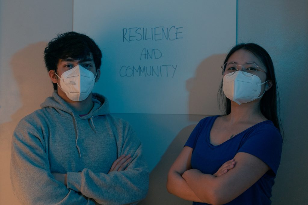 A masked man and woman standing in front of a poster, which says "resilience and community".