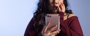 A woman holding a phone looking shocked.