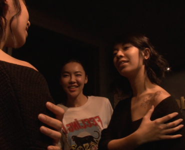 A woman showing off a new shoulder tattoo to two friends.