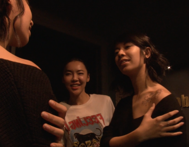 A woman showing off a new shoulder tattoo to two friends.