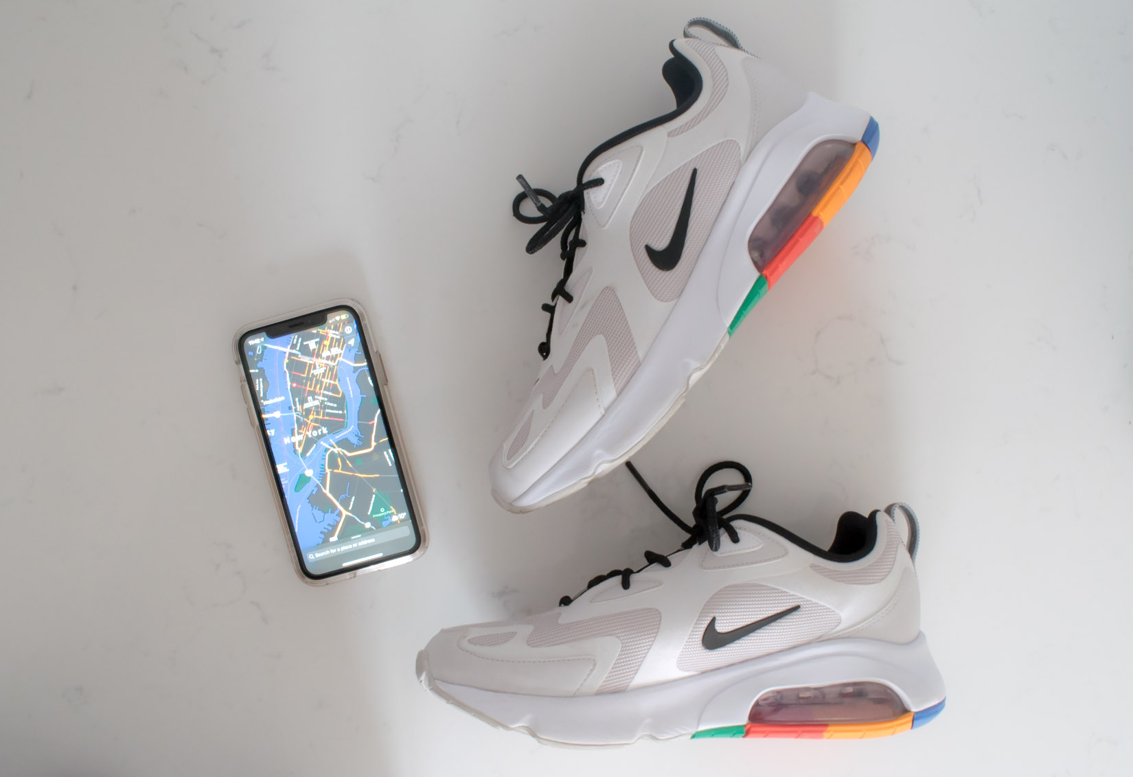 An overhead view of a pair of Nike sneakers set aside an iphone displaying a map on its screen