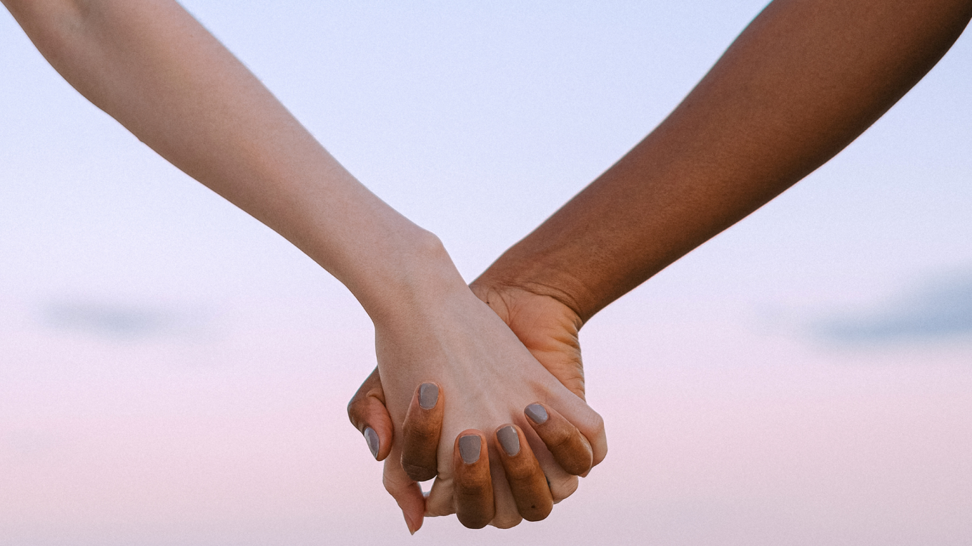 two arms holding hands with a pink sky background