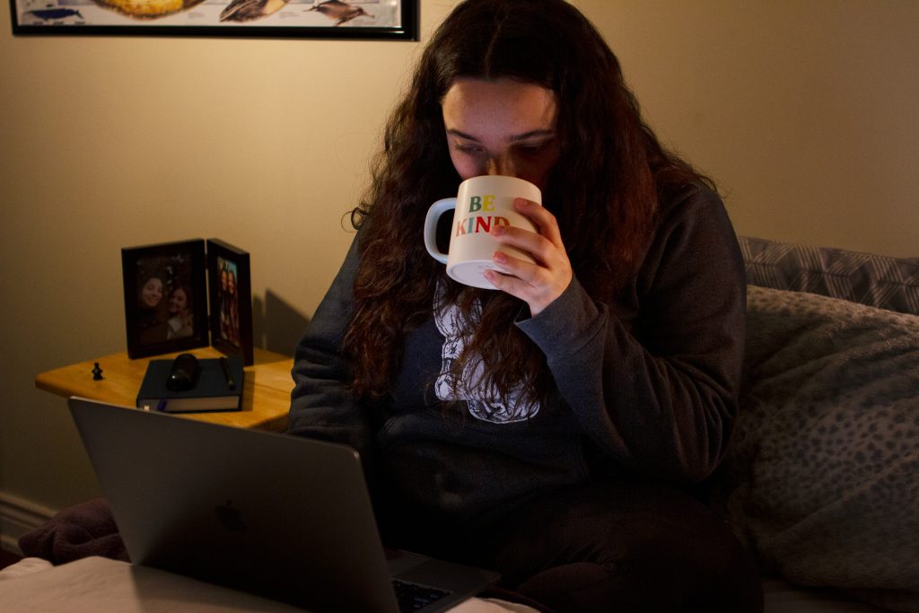 Girl sipping coffee in bed while on laptop