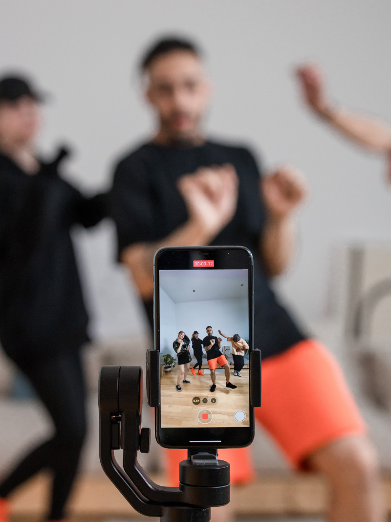 A phone displaying the tik tok camera app while people dance in frame.